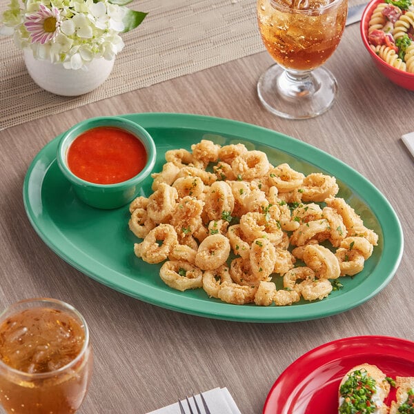 A green Acopa Foundations melamine oval platter with fried calamari, pasta, and dipping sauce on a table.