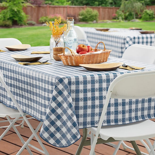 A picnic table with a Choice navy blue and white checkered vinyl table cover, set with a basket of fruit and a vase of flowers.