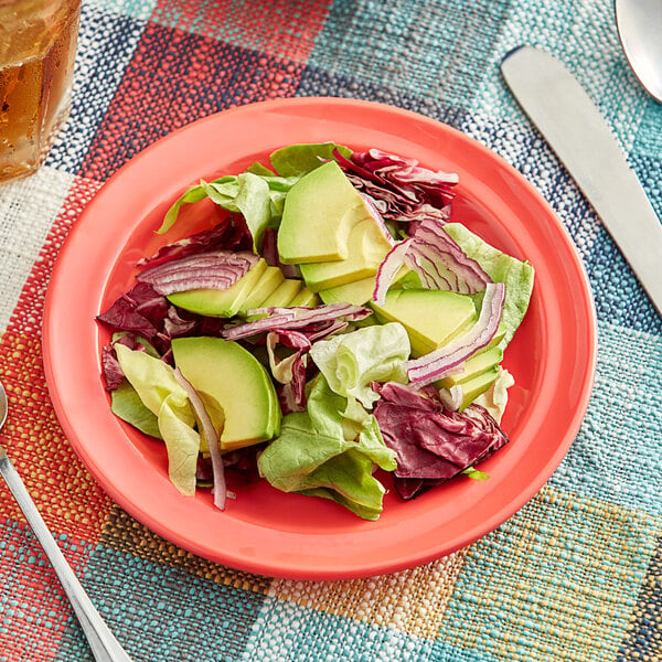 An Acopa Foundations orange melamine plate with a salad of avocado and lettuce on a table.