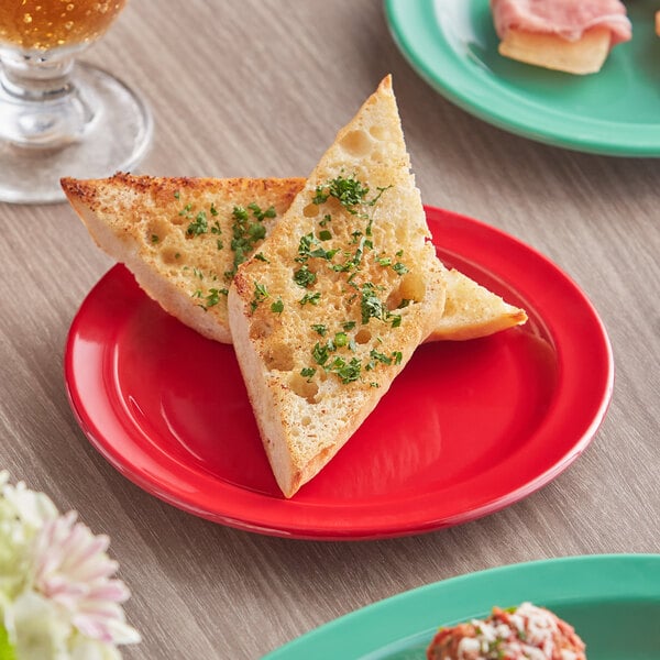 A piece of bread with green herbs on an Acopa red melamine plate.