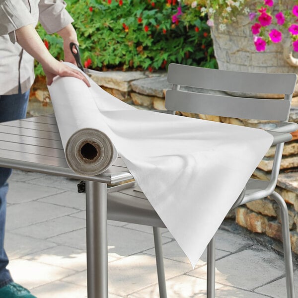 A woman cutting a white vinyl table cover roll on a table.