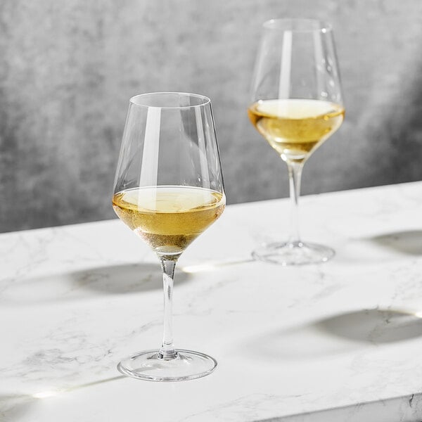 Two Della Luce Astro wine glasses filled with white wine on a marble table.