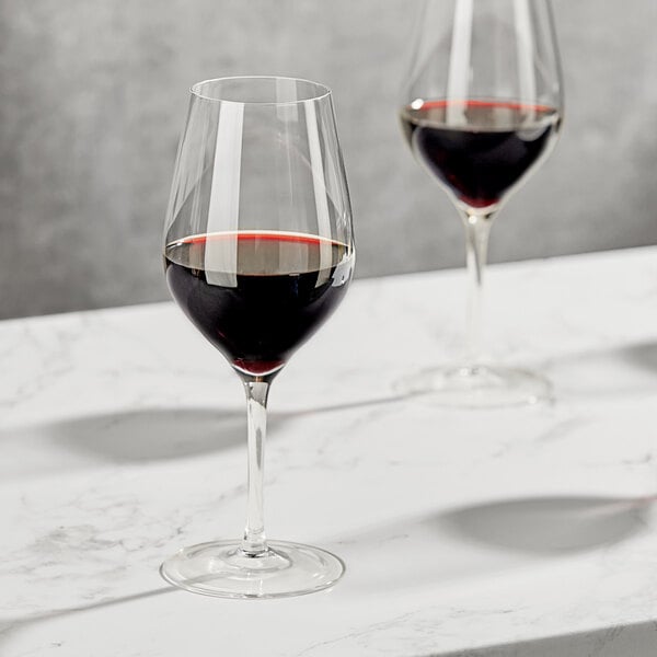 Two Della Luce Maia Bordeaux wine glasses filled with red wine on a marble surface.