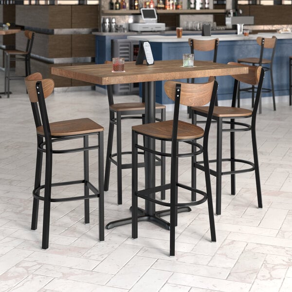 A Lancaster Table & Seating wood butcher block bar table with 4 chairs in a restaurant.