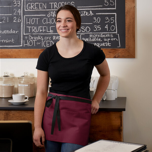 A woman wearing a black shirt and a burgundy waist apron with black webbing.