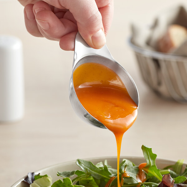 A person using a Vollrath stainless steel ramekin to pour sauce over a salad.