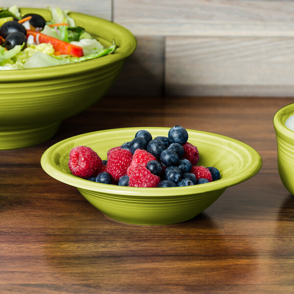 A green Fiesta china bowl filled with fruit and salad on a table.