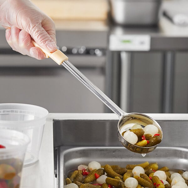 A gloved hand holding a Choice ivory perforated portion spoon full of food.