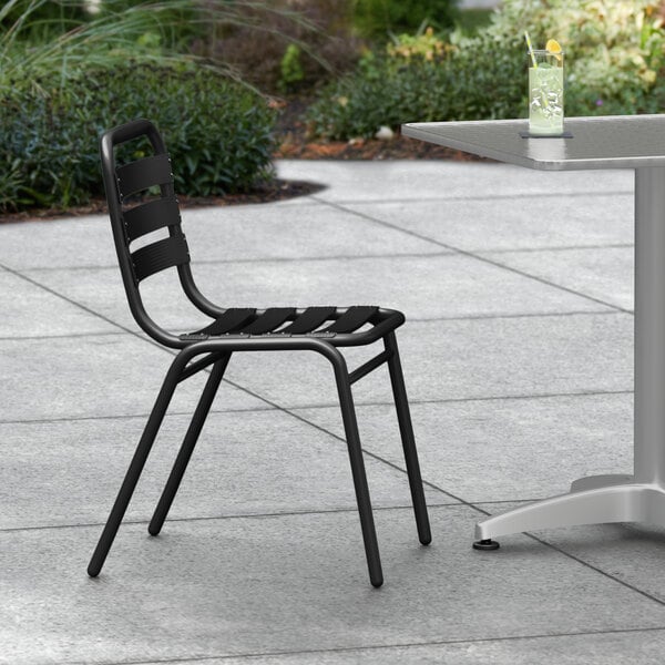 A black Lancaster Table & Seating outdoor chair on a sidewalk.