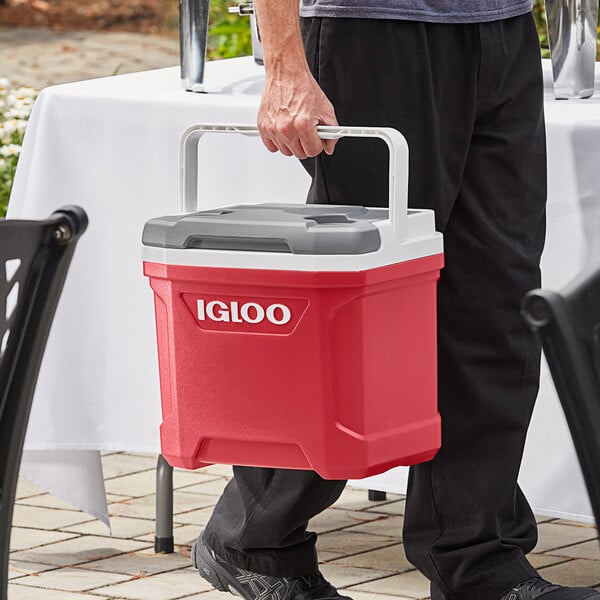 A person carrying a red and white Igloo cooler with a top swing handle.