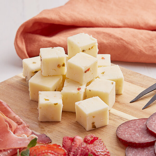 A cutting board with a block of Cabot Pepper Jack cheese, meat, and fruit.