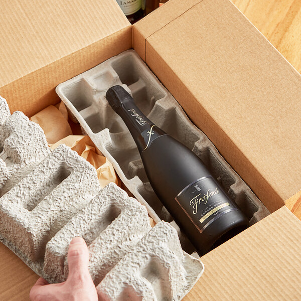 A person holding a bottle of wine in a Lavex Molded Fiber cardboard wine shipper tray.