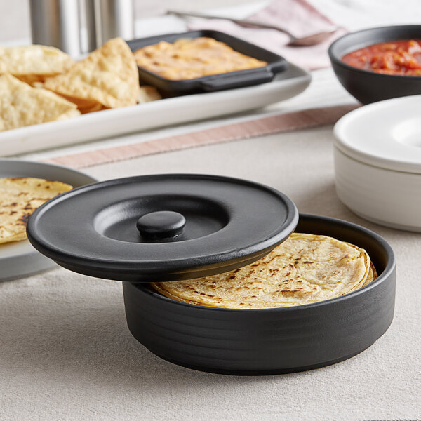 A black round Tuxton ceramic dish with tortillas inside.