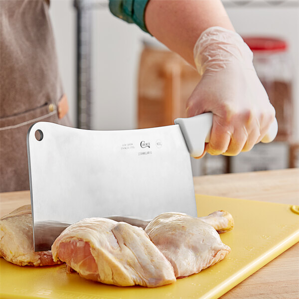 A person using a Choice 10" Cleaver to cut raw chicken on a yellow cutting board.