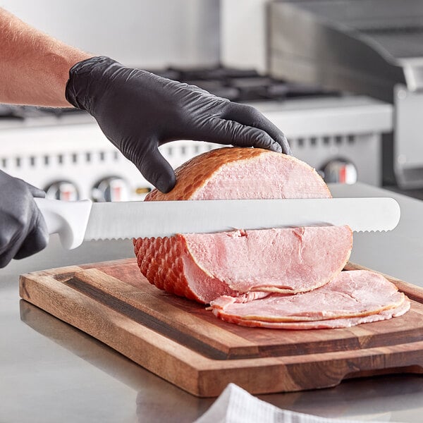 A person in black gloves using a Choice serrated slicing knife to cut ham on a cutting board.