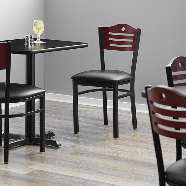 A Lancaster Table & Seating black bistro chair with a black vinyl seat and mahogany wood back on a table in a restaurant dining area.