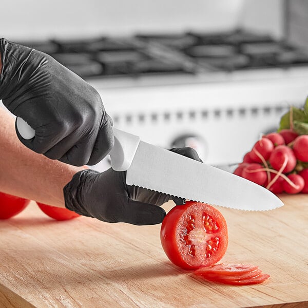 A person in black gloves using a Choice 8" Serrated Chef Knife to cut a tomato.