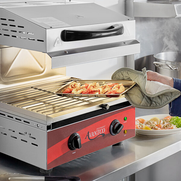 A person using an Avantco electric countertop salamander to cook food on a tray.
