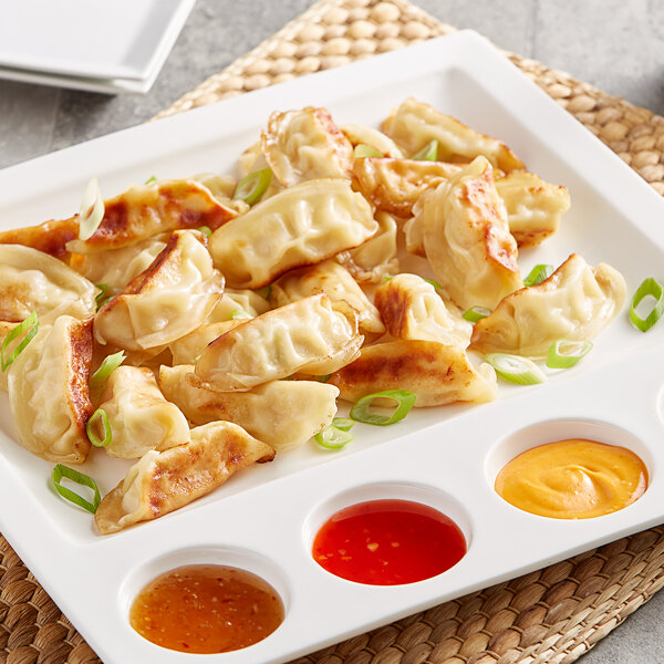 A white plate of Shrimp Gyoza dumplings with dipping sauce and green onions.