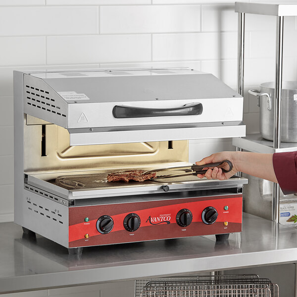 A person cooking food in an Avantco countertop salamander in a commercial kitchen.