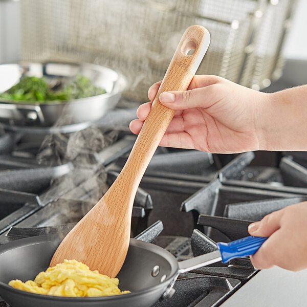 A person using an OXO wooden saute paddle to cook food in a pan.