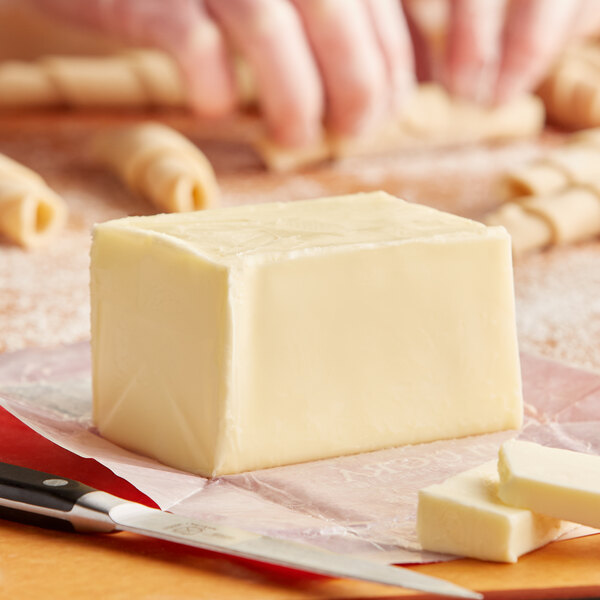 A person cutting a block of Plugra unsalted European butter on a cutting board.
