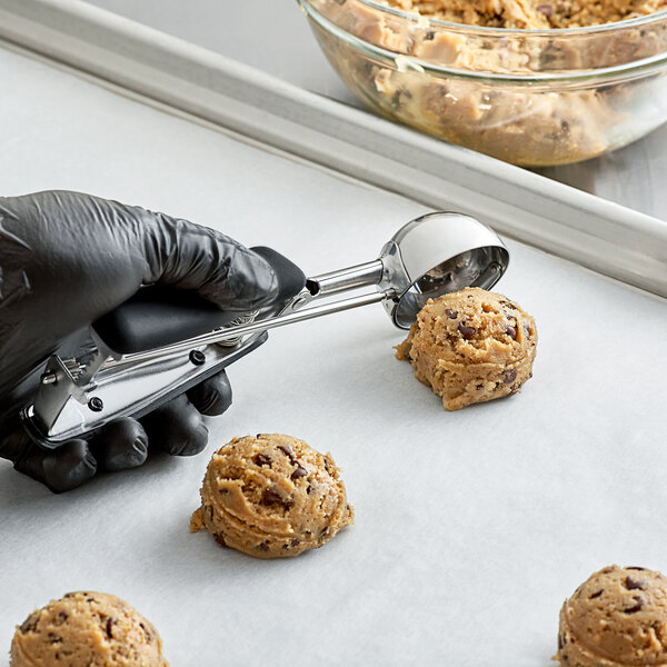 A person in gloves using an OXO Good Grips black squeeze handle disher to scoop cookie dough.
