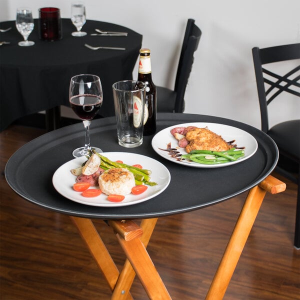 A black Cambro non-skid oval serving tray with food and wine glasses on a table.
