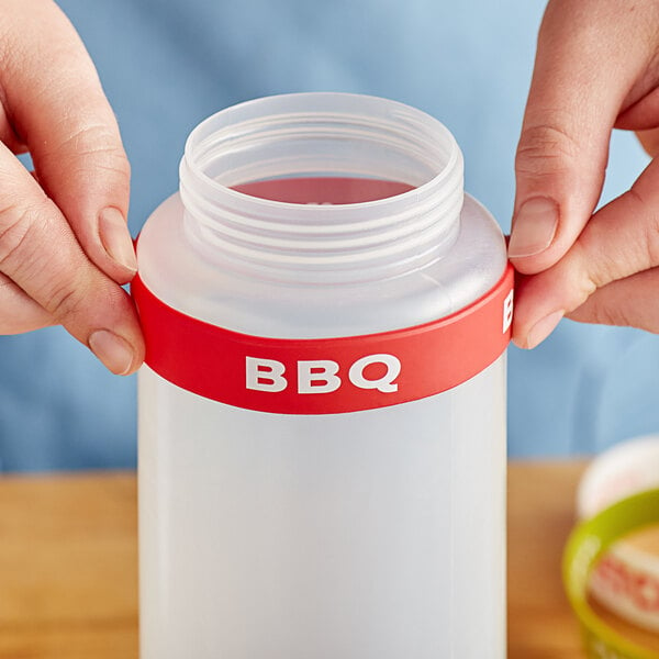 A person using a green and yellow BBQ silicone band on a plastic squeeze bottle.