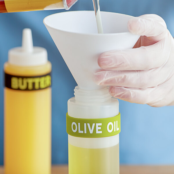 A person pouring olive oil into a funnel on a bottle of olive oil with a silicone label band.