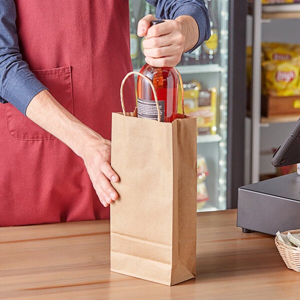 A hand holding a Choice natural Kraft paper shopping bag with a bottle of wine inside.