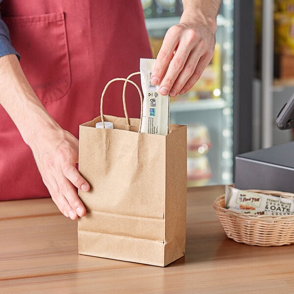 A person putting a packet into a brown natural kraft paper shopping bag with handles.