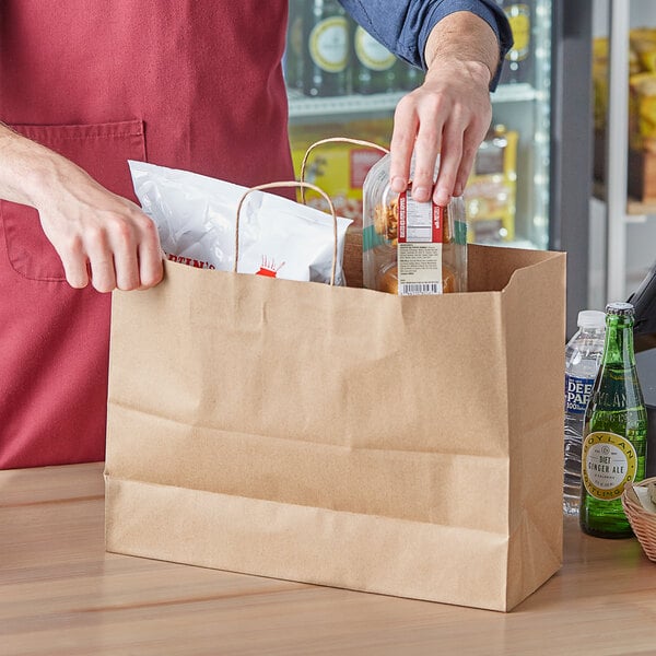 A man in a red apron putting food in a Choice natural kraft paper bag.