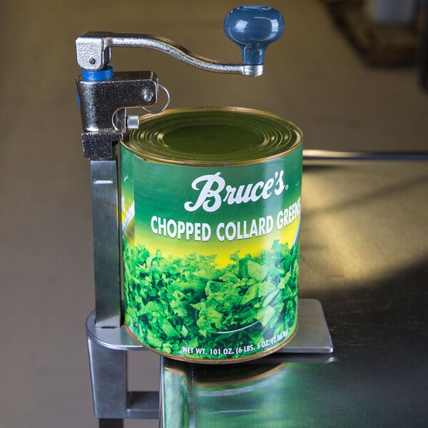 An Edlund Standard Duty Can Opener clamped to a metal stand opening a can of chopped collard greens.