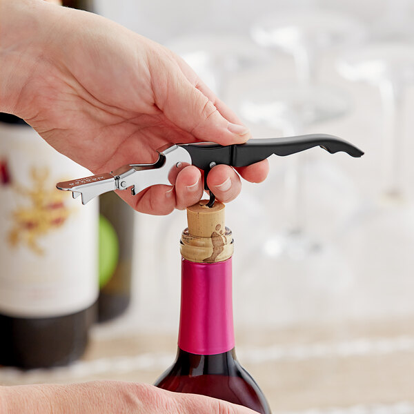 A hand using a Mercer Culinary waiter's corkscrew with a black and silver handle to open a bottle of wine.