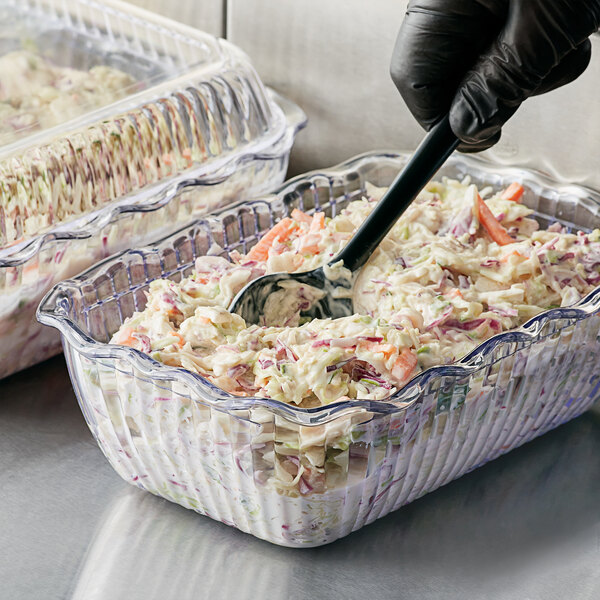 A person using a spoon to serve coleslaw from a Choice clear deli crock.