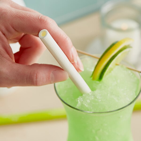 A person holding a Sorbos lime flavored paper straw in a glass of green liquid.