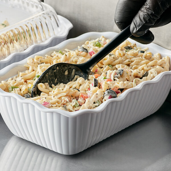 A gloved hand holds a black spoon in a white Choice deli crock filled with pasta.
