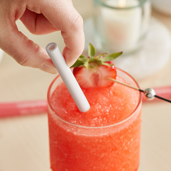 A person using a Sorbos strawberry flavored paper straw in a drink with a strawberry on top.