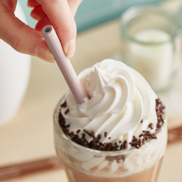 A person holding a Sorbos chocolate flavored paper straw in a glass of milkshake.