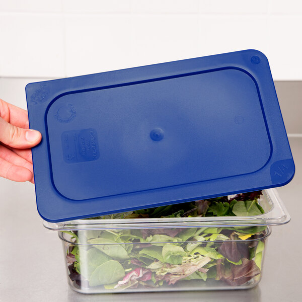 A hand using a blue Carlisle Smart Lid to cover a plastic container of salad.