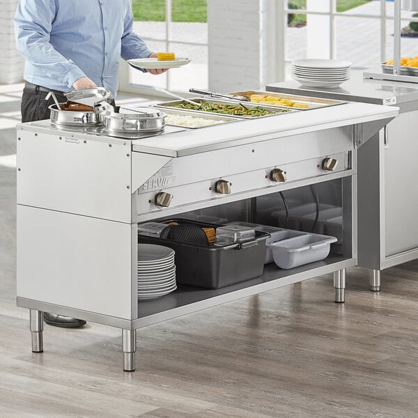 A man using a ServIt electric steam table on a large kitchen counter.