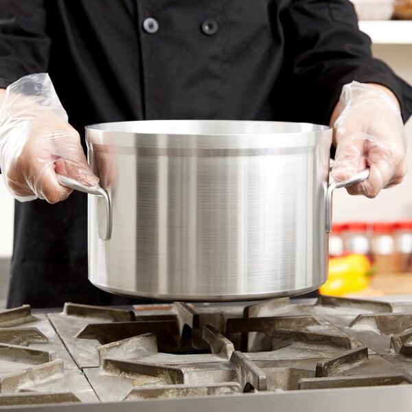 A chef in gloves using a Vollrath Wear-Ever stock pot over a stove.