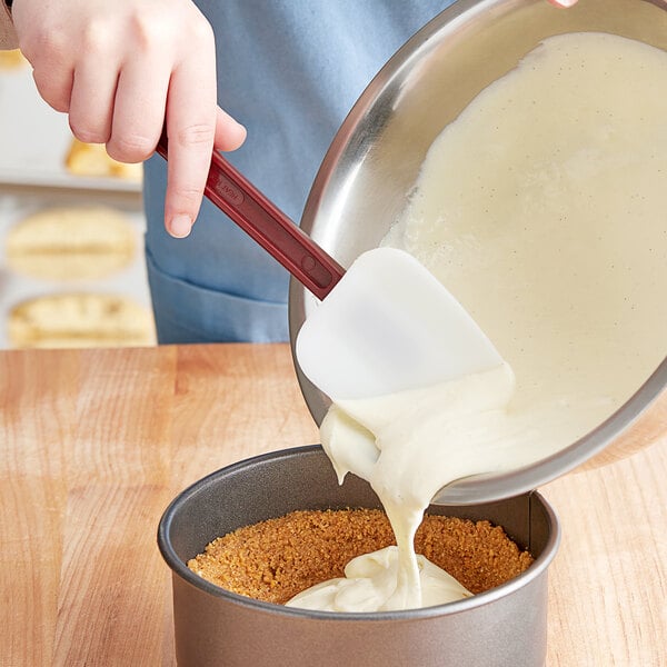A red Choice spoonula pouring white cake batter into a pan.