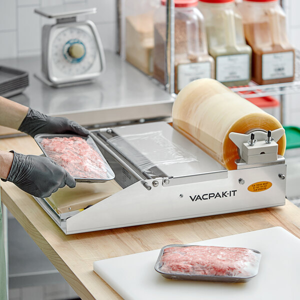 A VacPak-It film wrapping machine with plastic wrap on the counter in a butcher shop.