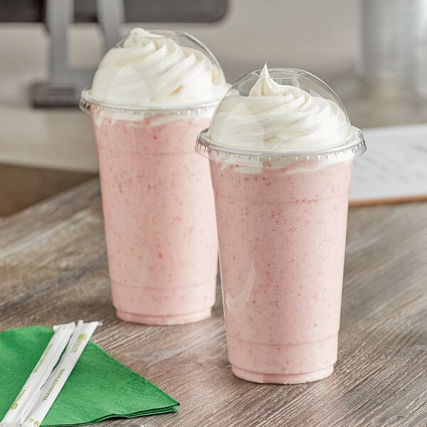 Two Choice clear plastic cups with dome lids and straws on a table.