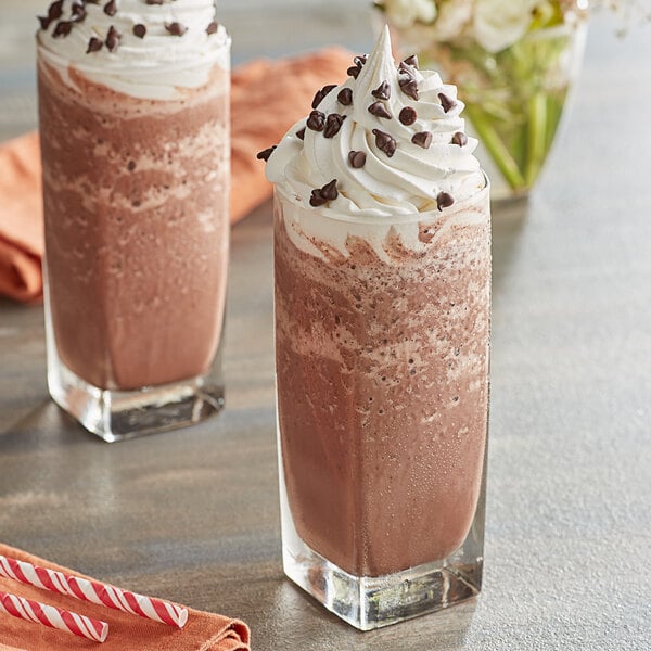 Two glasses of Ghirardelli dark chocolate milkshakes with whipped cream and chocolate chips.