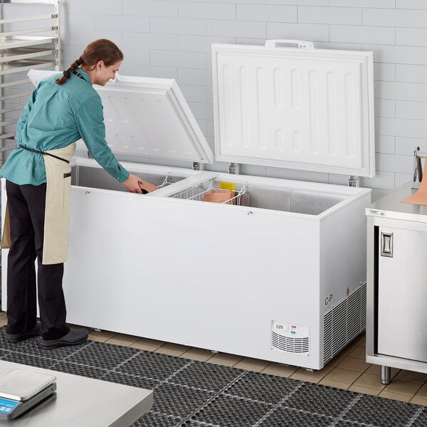 A woman opening the white door of a Galaxy commercial chest freezer in a professional kitchen.