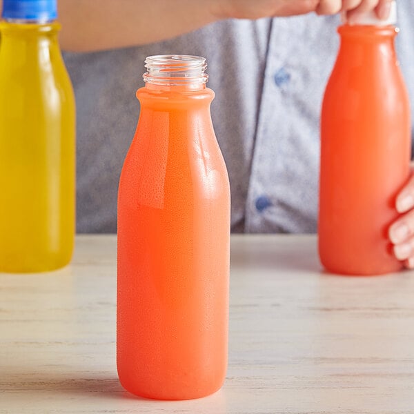 A person holding a 16 oz. clear PET juice bottle with orange liquid.