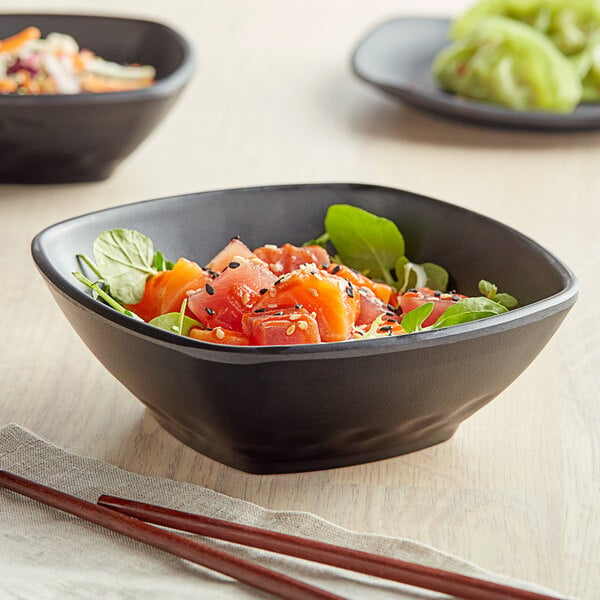 A table with two black square melamine bowls filled with food and chopsticks.